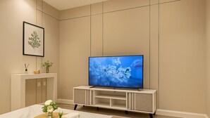A modern living room with a flat-screen TV on a minimalist stand, a white coffee table with decorative items, and a neutral color scheme. - EWA Host (Riyadh)