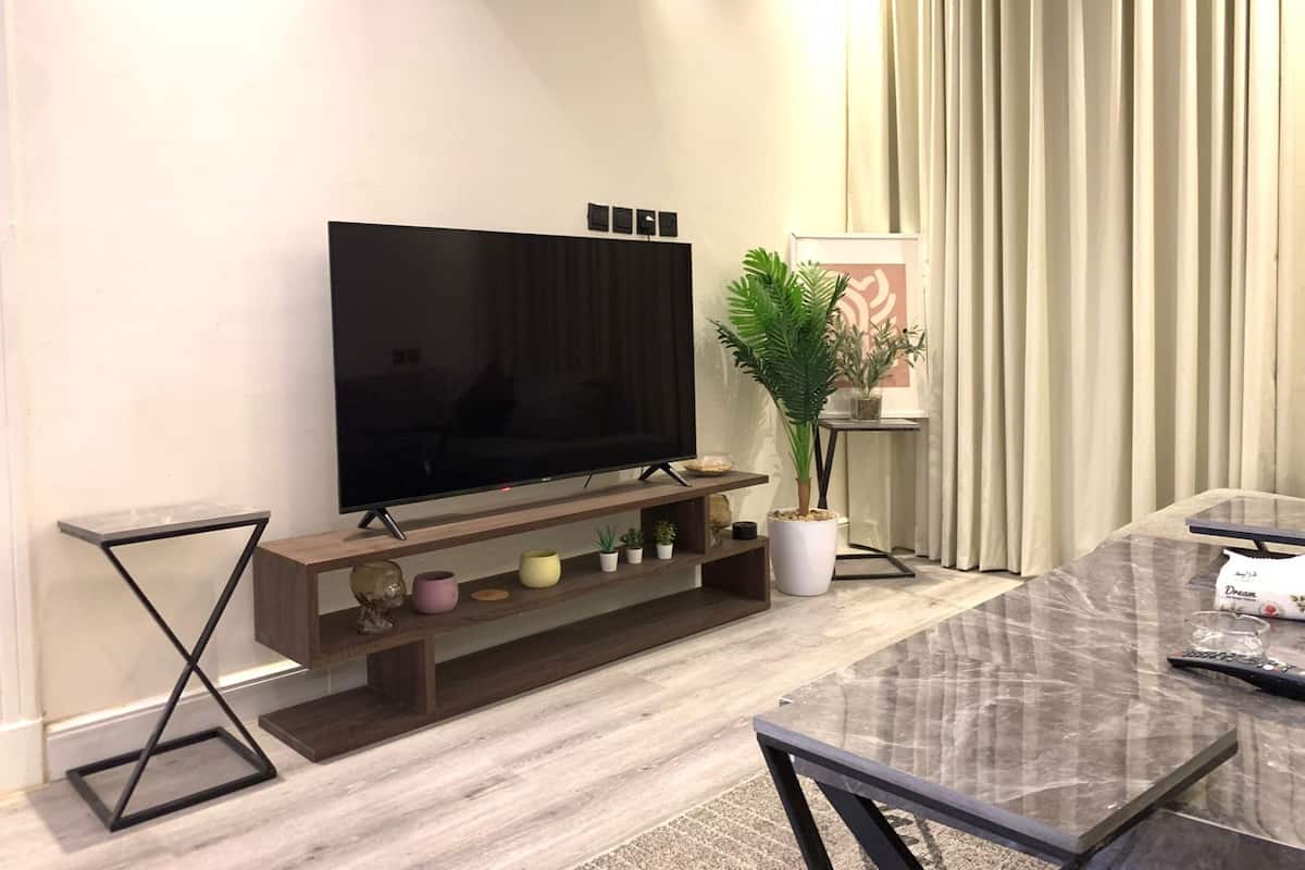 Un salon moderne avec un grand téléviseur à écran plat posé sur un meuble en bois, une table à manger avec des chaises et une plante en pot.