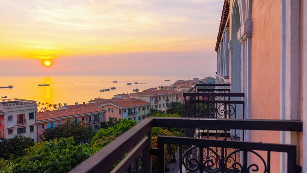 A balcony with wrought iron railings overlooking a coastal cityscape at sunset. - Lotus Home Cafe - Signature (Phu Quoc)