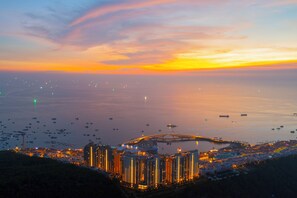 A coastal cityscape at dusk with illuminated buildings, a bridge, and boats on the water. - Lotus Home Cafe - Signature (Phu Quoc)