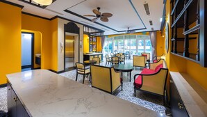 A hotel lobby with a marble reception desk, yellow walls, and a dining area with wicker chairs and a red sofa. - Lotus Home Cafe - Signature (Phu Quoc)