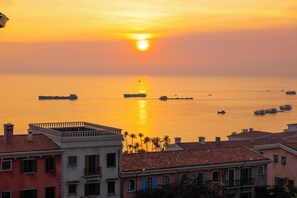 A coastal cityscape at sunset with buildings and boats on the water. - Lotus Home Cafe - Signature (Phu Quoc)
