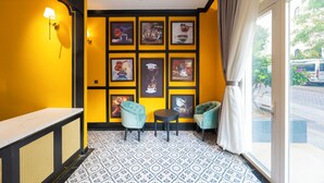 A room with a yellow wall, a black and white patterned floor, and a series of framed pictures on the wall. There are two chairs and a small table. - Lotus Home Cafe - Signature (Phu Quoc)