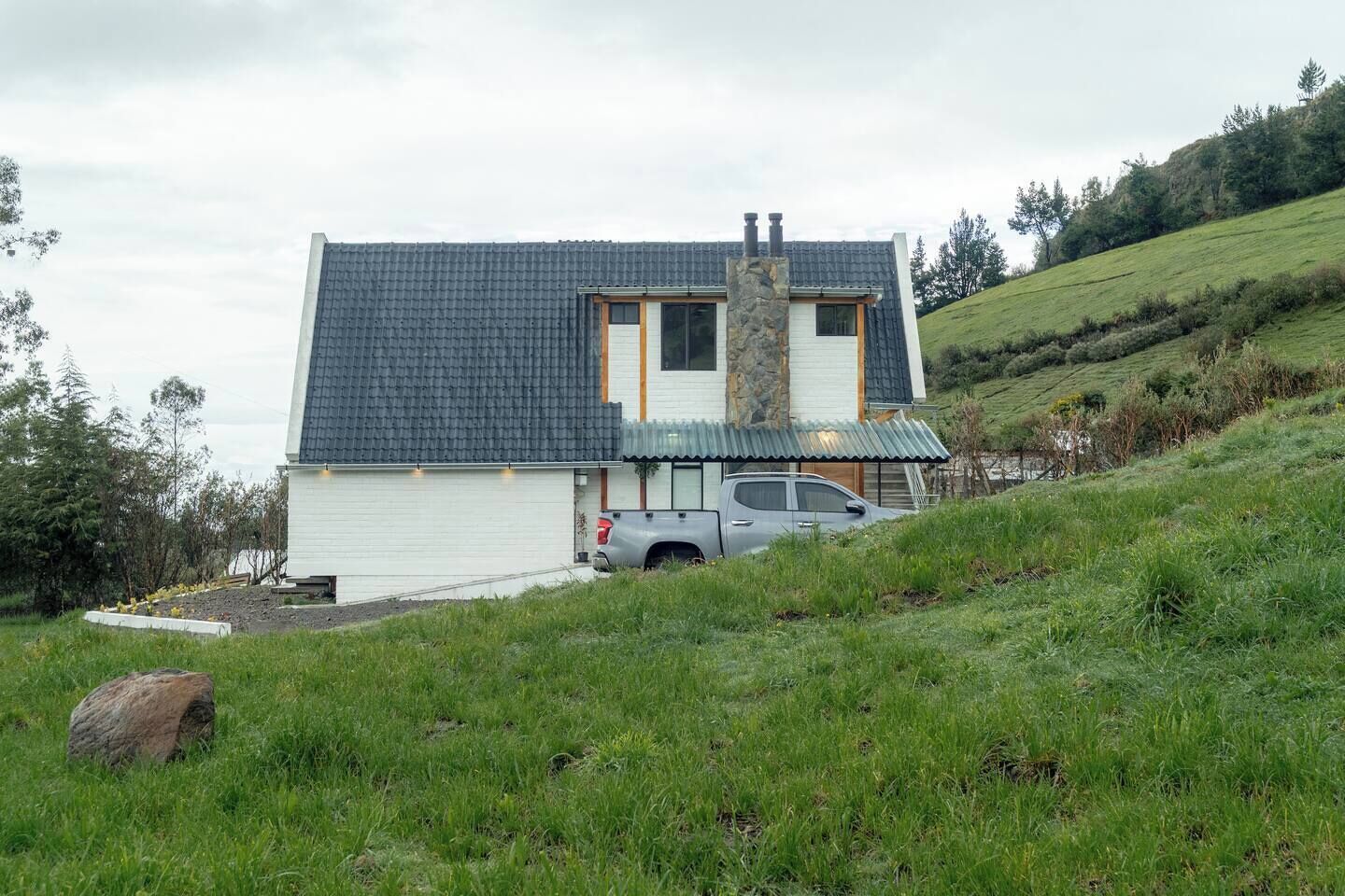 A modern house with a sloped roof, a stone chimney, and a garage with a truck parked outside.