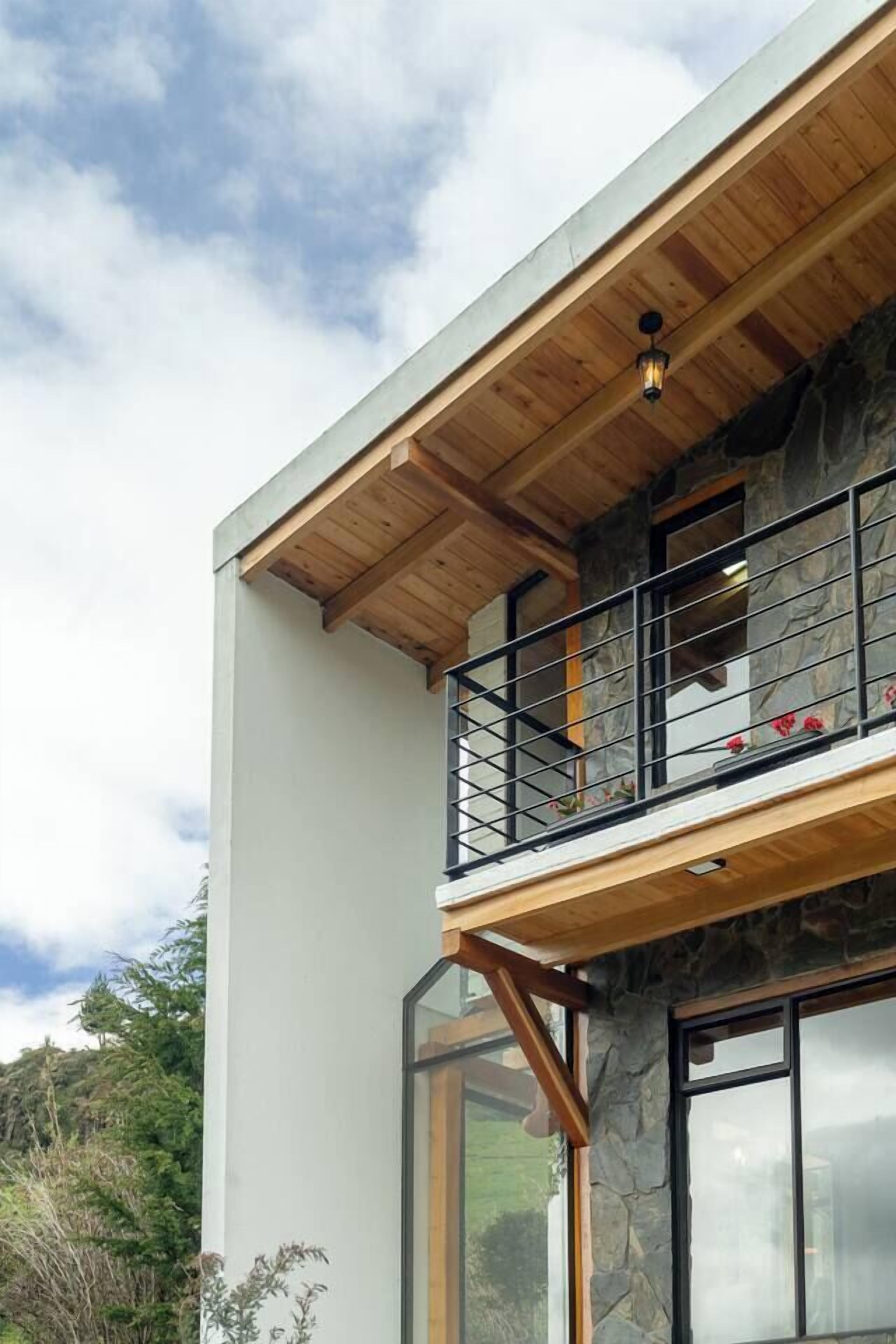Un edificio moderno de dos pisos con balcón, fachada de piedra y ventanas amplias.