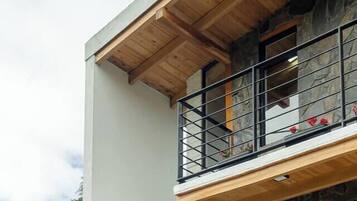 Un edificio moderno de dos pisos con balcón, fachada de piedra y ventanas amplias.