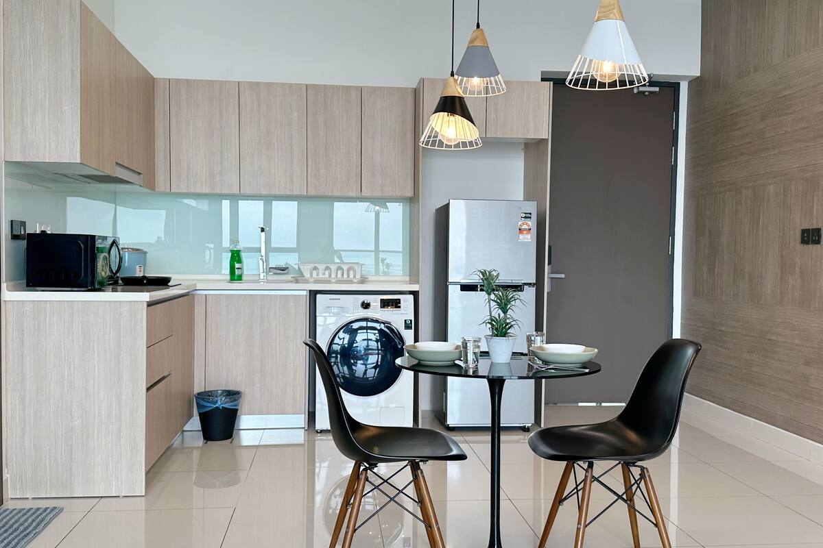 A modern kitchen with wooden cabinets, a built-in dishwasher, a refrigerator, and a dining area with two black chairs and a round table.