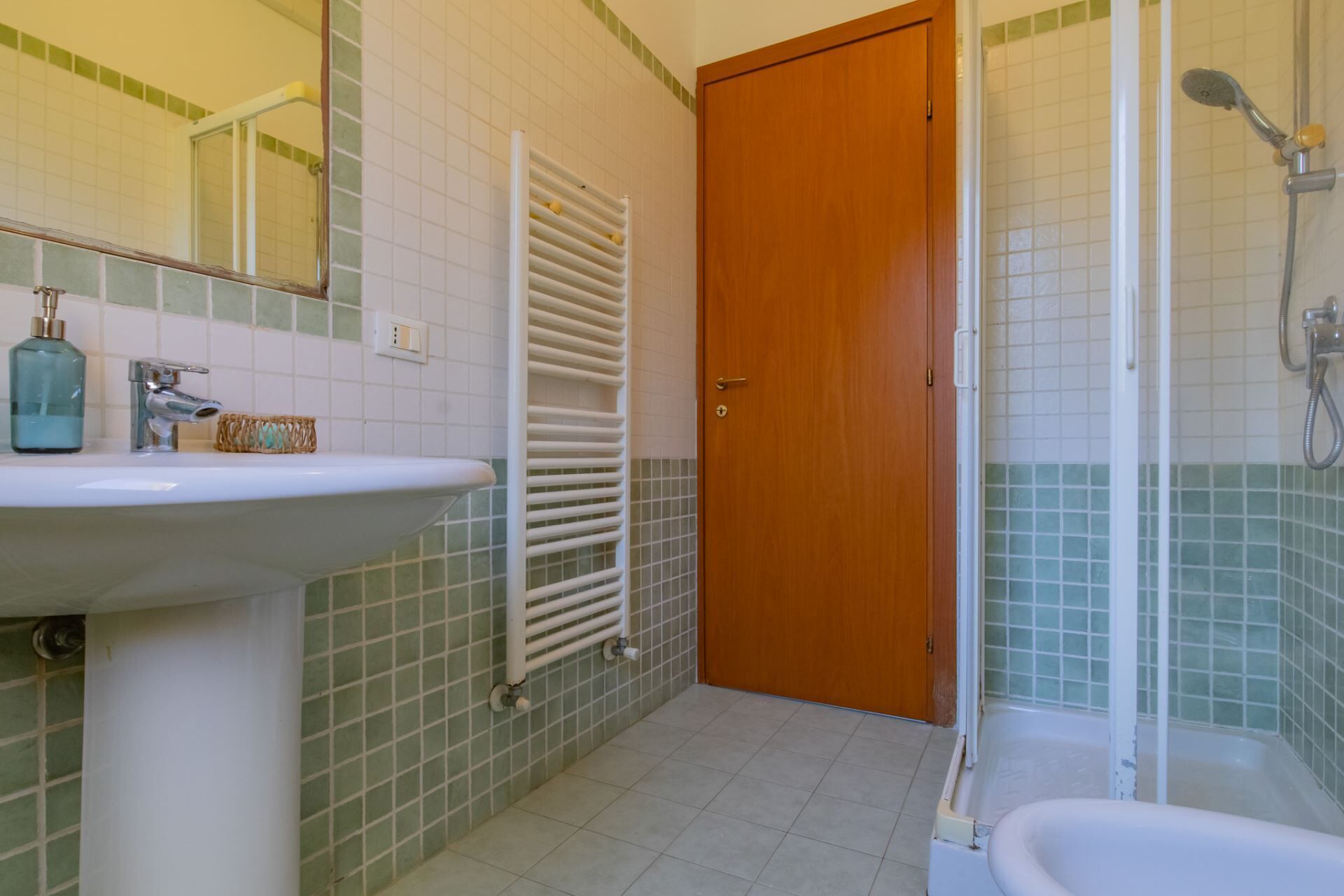 Une salle de bain comprenant un lavabo, un miroir, un porte-serviettes, une douche et une porte.