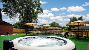 An outdoor hot tub surrounded by lawn chairs and picnic tables under umbrellas, with a wooden fence and houses in the background. - Spacious 5-bedroom house with Jacuzzi, Game room & WIFI in delightful Southfield (Southfield)