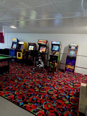 Una habitación con máquinas de videojuegos, mesa de billar y una alfombra colorida.