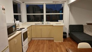 A compact kitchen with a microwave, stove, and sink, a small dining table, and a sofa in a corner.