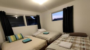 A room with three single beds, each with a different patterned bedspread. There are windows with black curtains, and the room has a wooden floor.