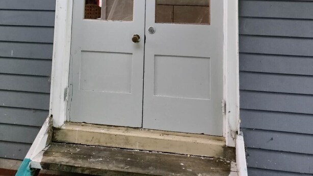 A white double door with a small window, set in a gray siding house.