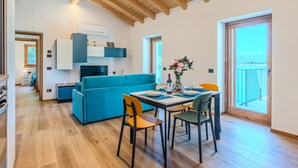 A modern living room with a blue sofa, dining table, and chairs, wooden flooring, and a balcony with a view. - Apartment Svasso by Interhome (Lago di Mezzola)