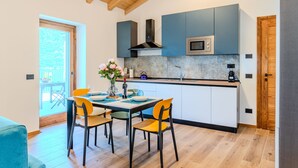 A modern kitchen with wooden beams, a dining area with a table set for four, and a view of the outdoors. - Apartment Svasso by Interhome (Lago di Mezzola)