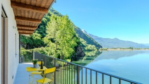 A balcony with a yellow table and chairs, overlooking a calm lake and green mountains.