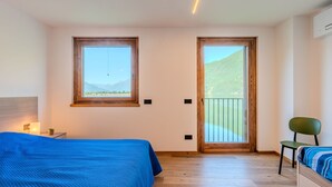 A bedroom with a bed, a chair, a nightstand, and a window with a view of a lake and mountains.