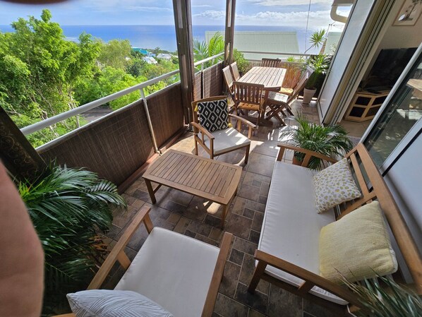 A balcony with wooden furniture, including a table and chairs, and a sofa.