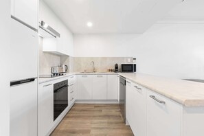 A modern kitchen with white cabinetry, a wooden floor, and a marble countertop. - Camperdown Cozy Corner 8 (Sydney)