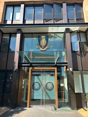 The entrance to St John's College with a prominent crest above the doors and the name 'HINTZE BUILDING' on the glass facade. - Camperdown Cozy Corner 8 (Sydney)