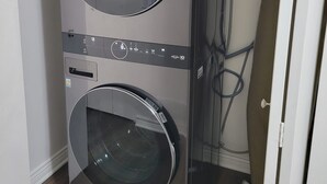 Une machine à laver et un sèche-linge superposés dans une pièce dont le sol est en bois et la porte est blanche.