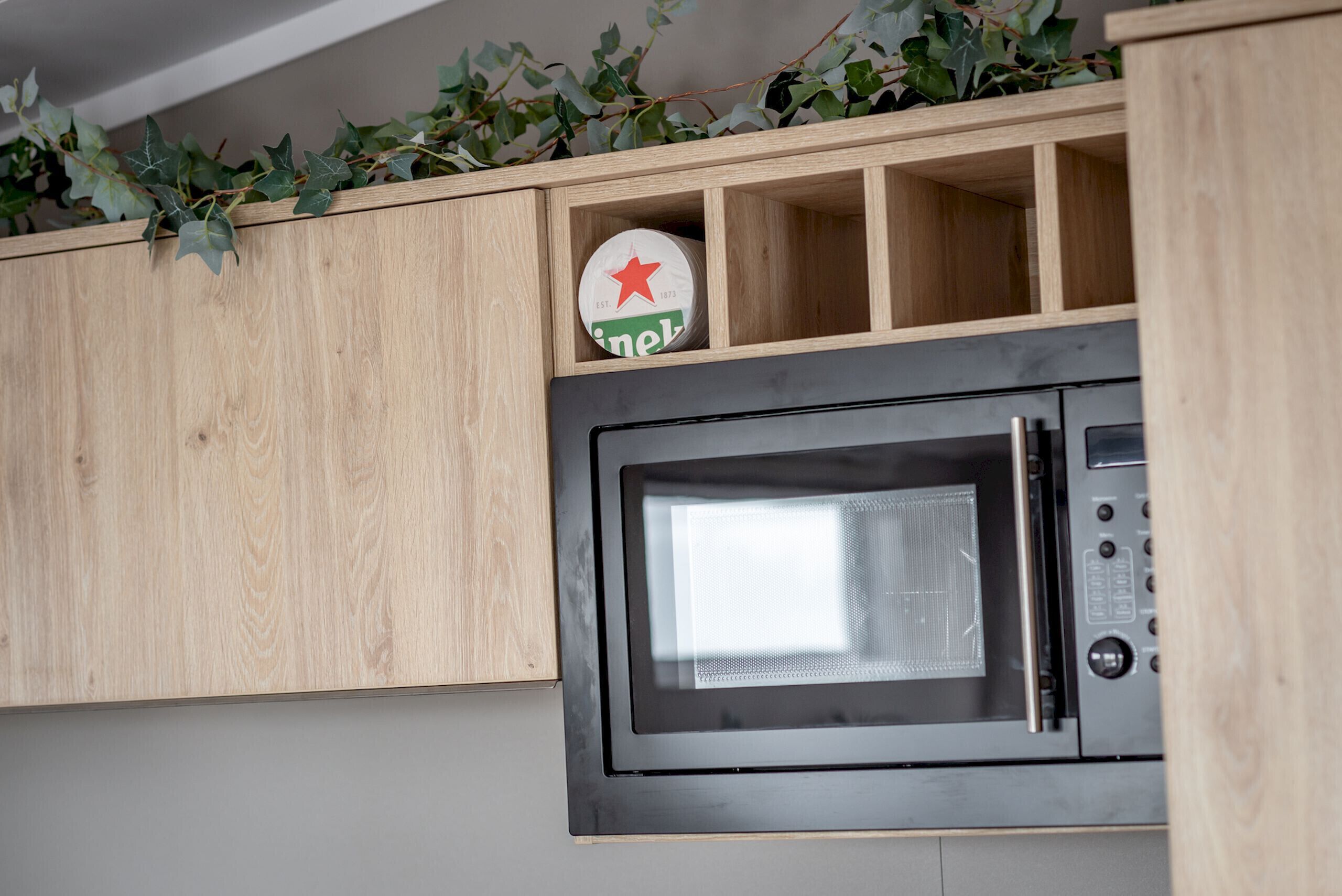 Una cocina con microondas y una estantería con una lata de cerveza Heineken.