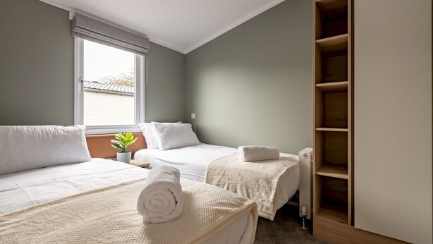 A hotel room with two beds, a large window, a radiator, and a wooden wardrobe.