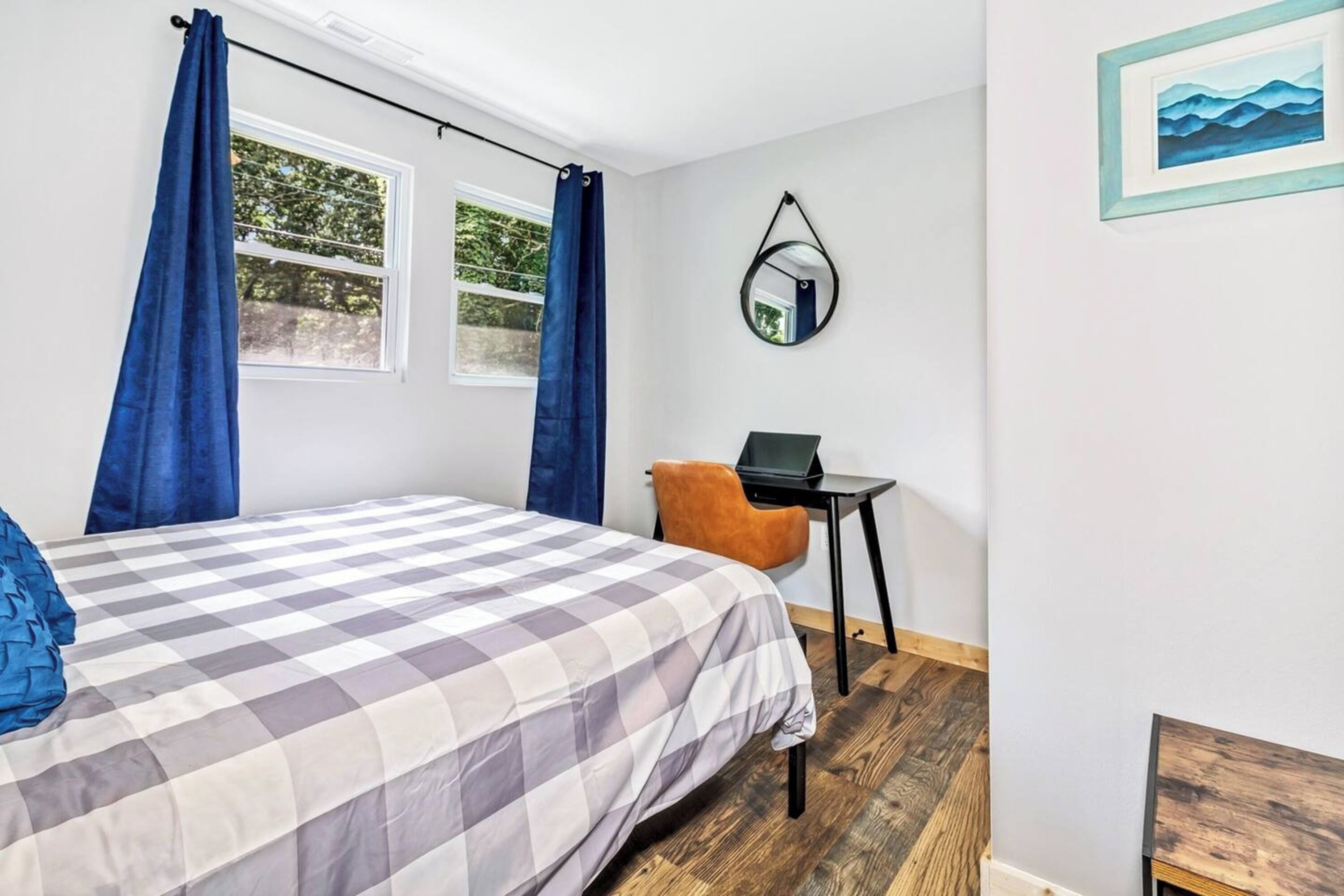A bedroom with a bed, a desk, a chair, a mirror, and a window with curtains.