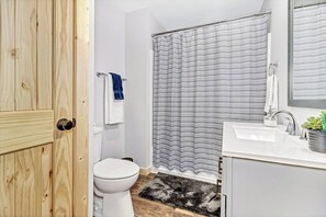 A bathroom with a white toilet, a shower with a striped curtain, a sink with a mirror, and a wooden door. - Bear Walk Cottage in Black Mountain (Black Mountain)