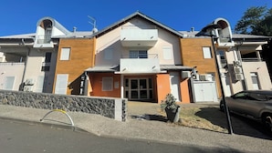 A modern multi-story building with a central entrance, balconies, and air conditioning units.