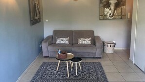 A living room with a grey sofa, two side tables, a patterned rug, and wall art including an elephant painting.