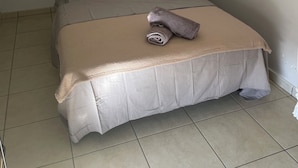 A small, single-bed room with a sloped ceiling, a beige bedspread, and a rolled-up towel on the bed.
