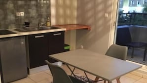 A compact kitchen with a built-in oven, a sink, and a countertop. There is a dining table with two chairs and a patterned rug.