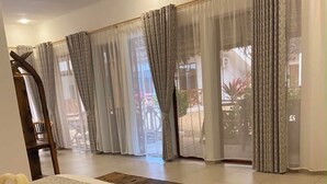 Ein Hotelzimmer mit einem Bett, einer Holzbank und großen Fenstern mit Vorhängen.