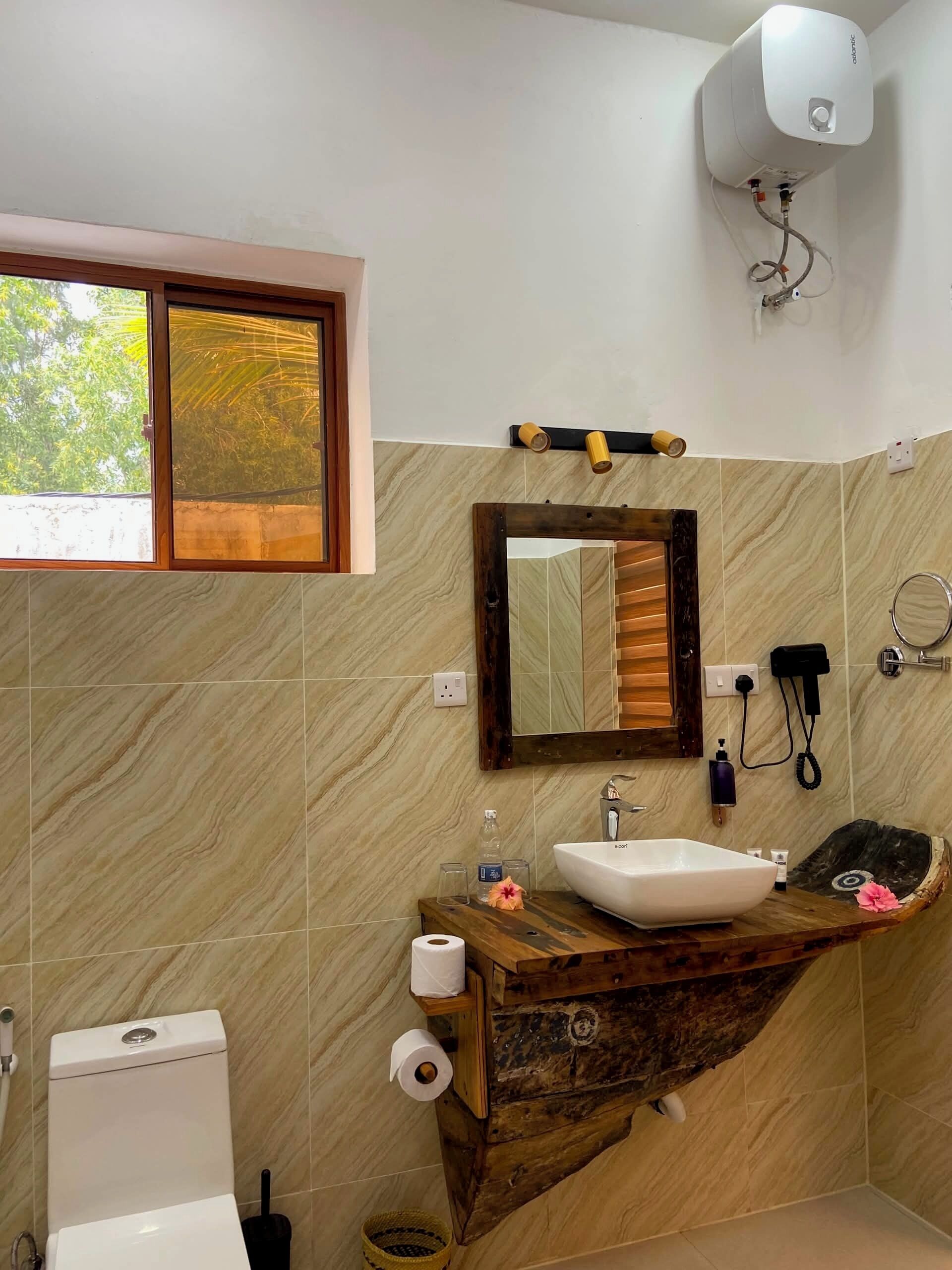 A bathroom with a toilet, sink, mirror, and window.