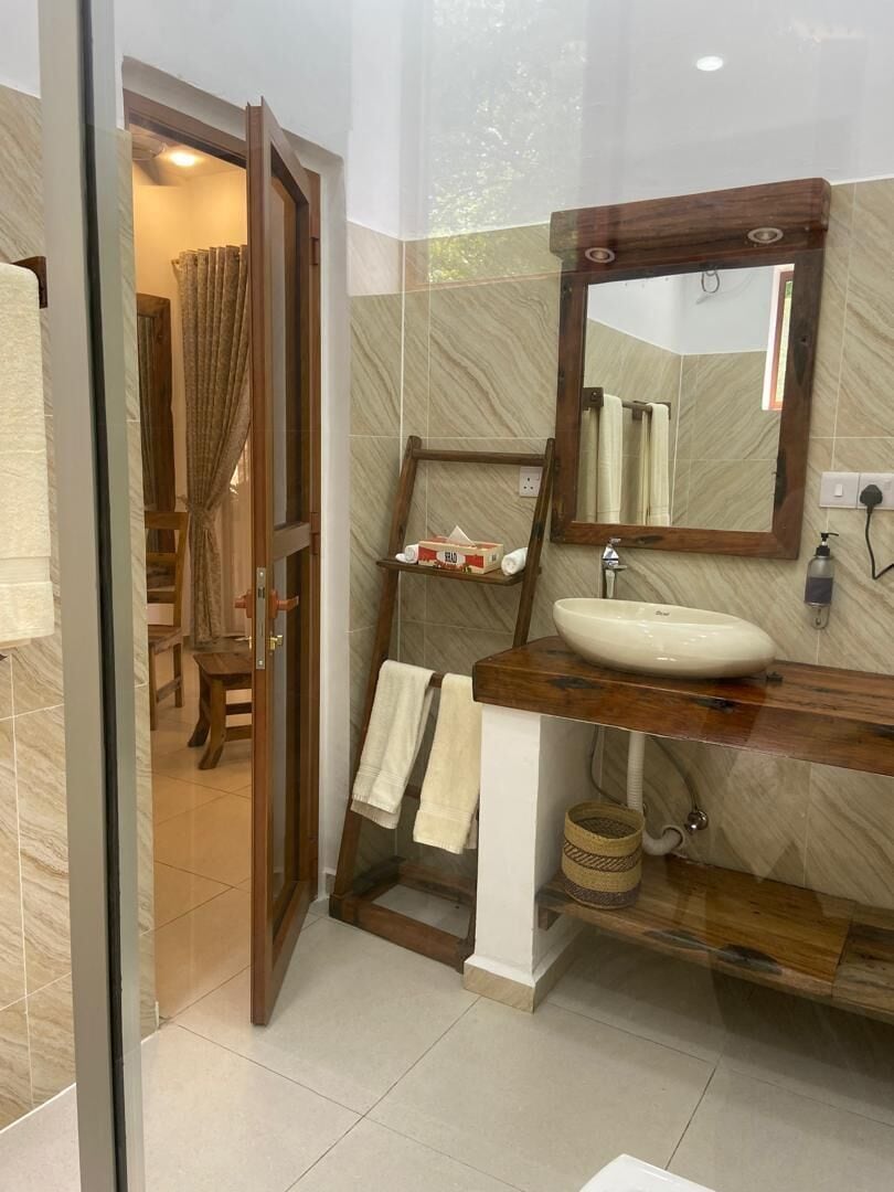 Un baño con tocador de madera, un espejo grande y una puerta de cristal que da a la zona de la ducha.