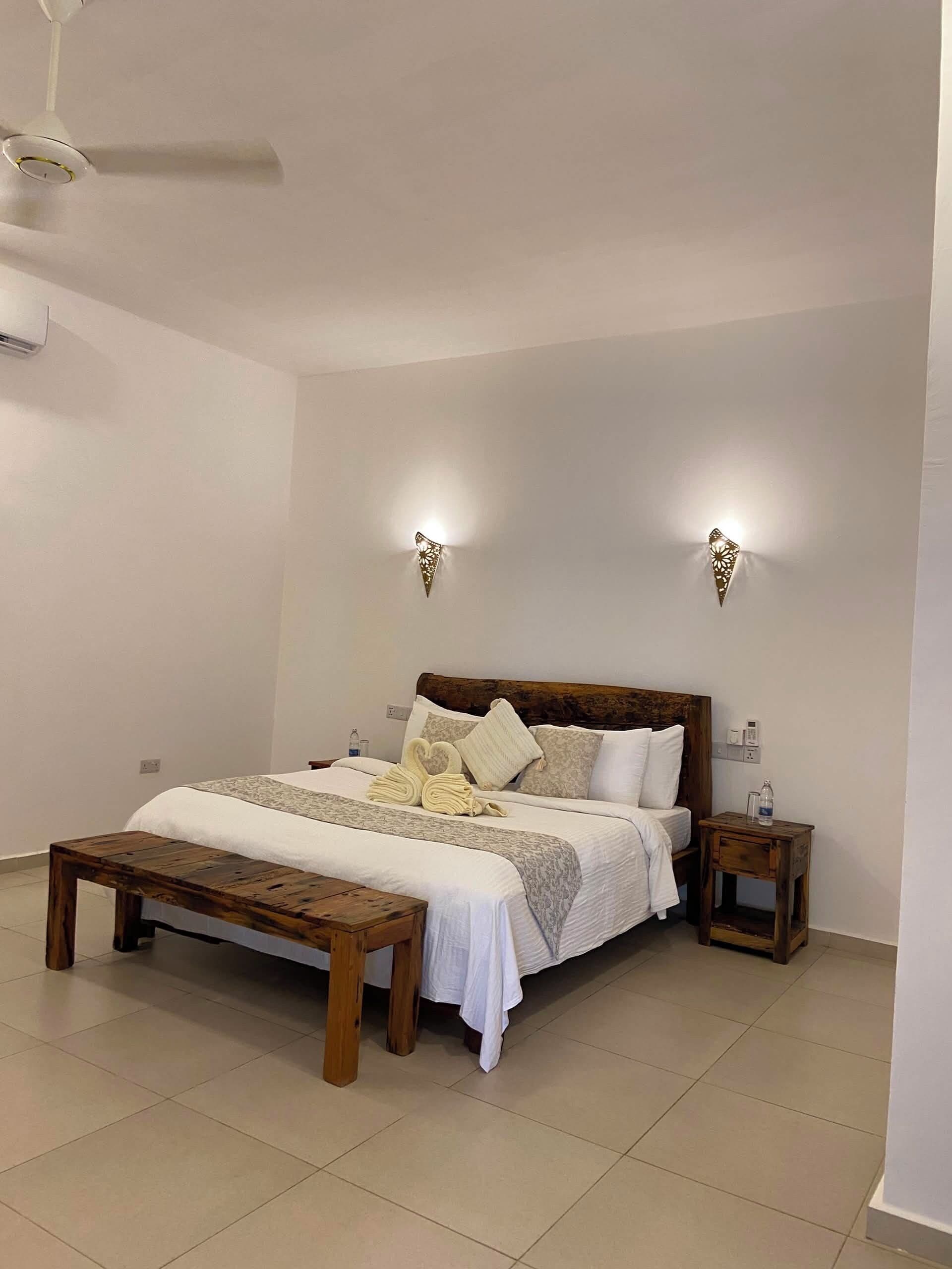 A neatly arranged bedroom with a bed, bedside tables, a wooden bench, and a ceiling fan.