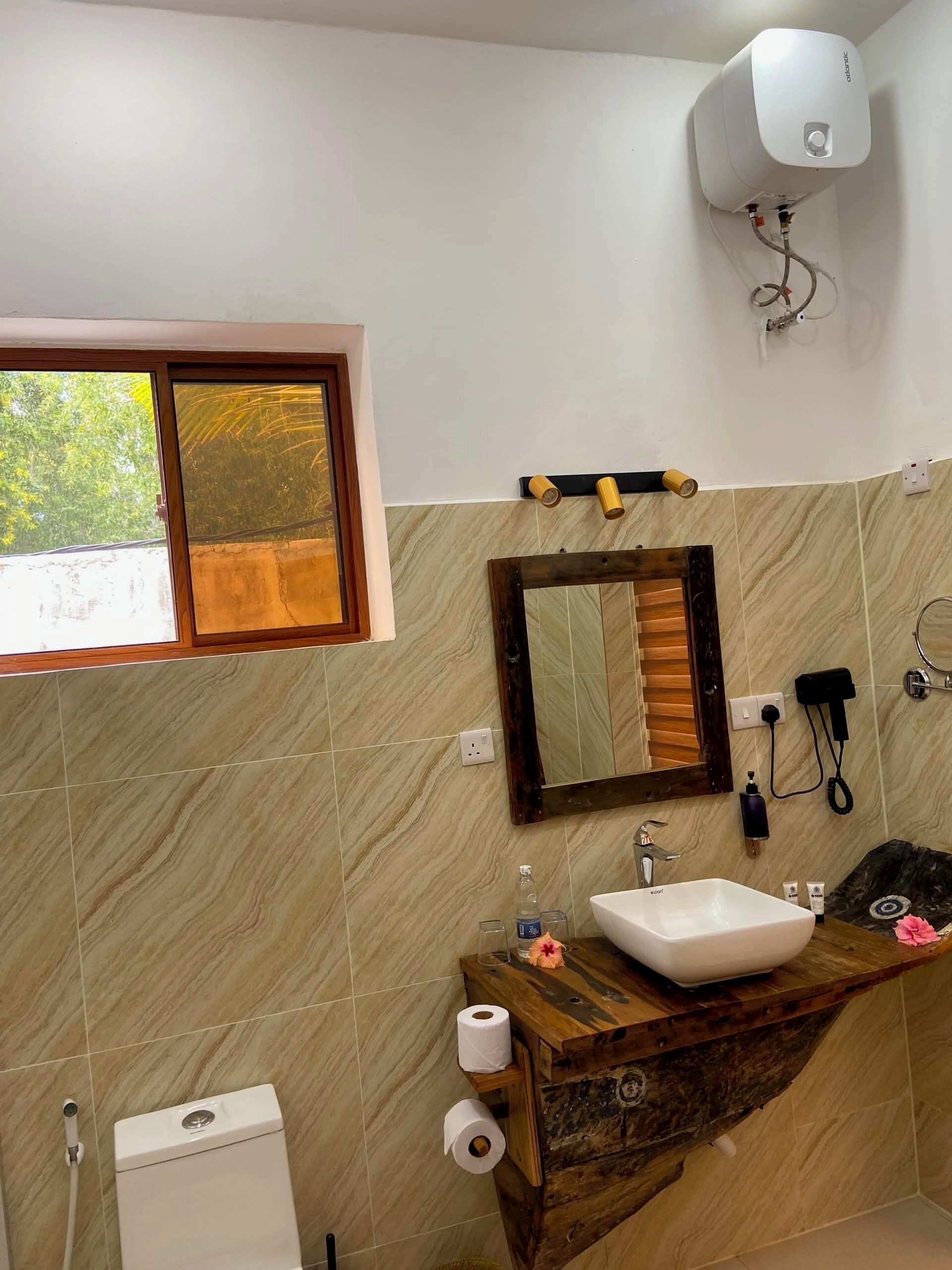 A bathroom with a toilet, sink, mirror, window, and a wall-mounted heater.