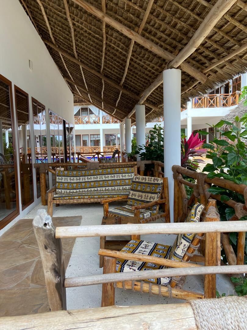 A covered outdoor seating area with wooden furniture and a thatched roof.
