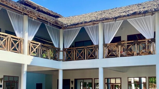 Ein mehrstöckiges Hotel mit Pool, Holzbalkonen und weißen Vorhängen.