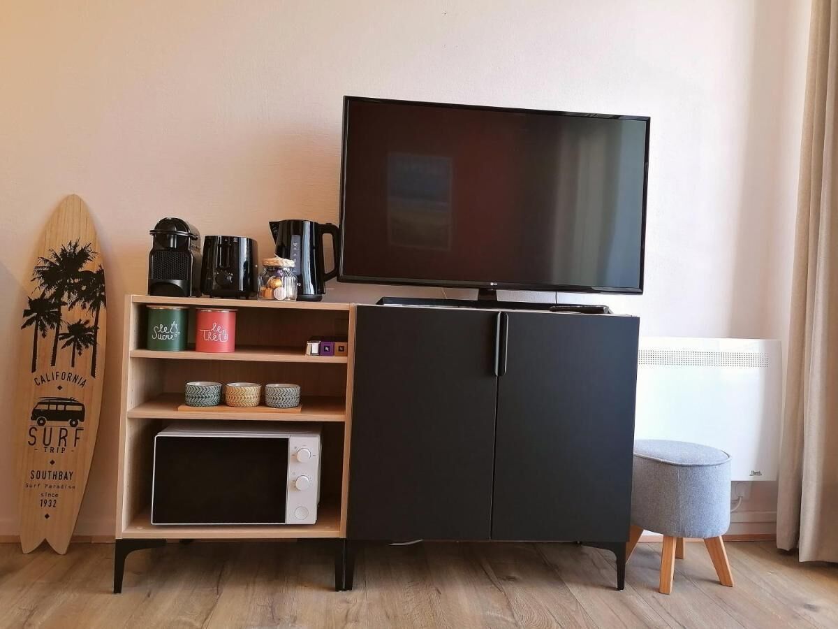 A room with a black TV stand, a surfboard, and a small grey ottoman.