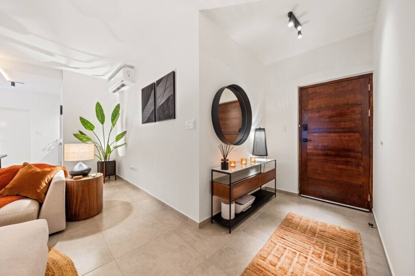 Ein modernes Wohnzimmer mit einer Couch, einem Couchtisch, einer Pflanze, einem Konsolentisch mit Dekoration und einer großen Holztür.