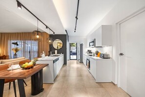 Una cocina moderna con armarios blancos, una isla central y un comedor con mesa y sillas de madera.