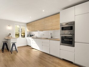 Cozinha moderna com armários brancos, forno duplo e bancada de madeira.