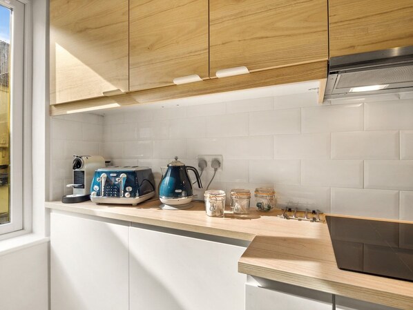Une cuisine avec des meubles blancs, un plan de travail en bois, une machine à café, un grille-pain et des bocaux.