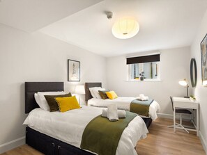 A hotel room with two beds, a desk, a chair, a window with a view, and a ceiling light. - The Town Place @ Clifden Boutique Apartments (Clifden)