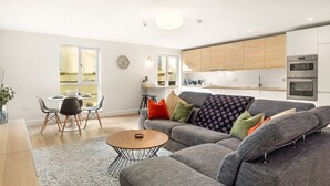 Een moderne woonkamer met een grijze bank, een ronde salontafel en een eethoek met een witte tafel en stoelen.