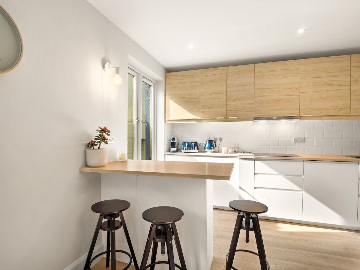 Una cucina moderna con mobili in legno, un piano di lavoro bianco e tre sgabelli.