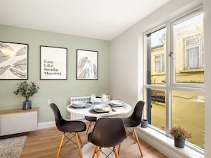 A dining area with a round table set for four, two black chairs, a vase with flowers, and framed artwork on the wall. - The Town Place @ Clifden Boutique Apartments (Clifden)