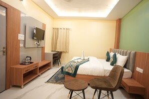 A hotel room with a bed, a desk, a chair, a TV, and a small table. - Heaven Heritage (Varanasi)